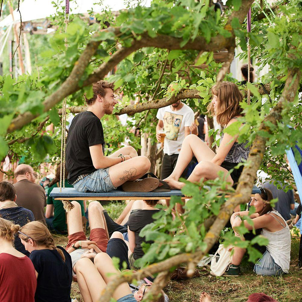 Menschen sitzen auf einer Schaukel im Baum, umgeben von Publikum