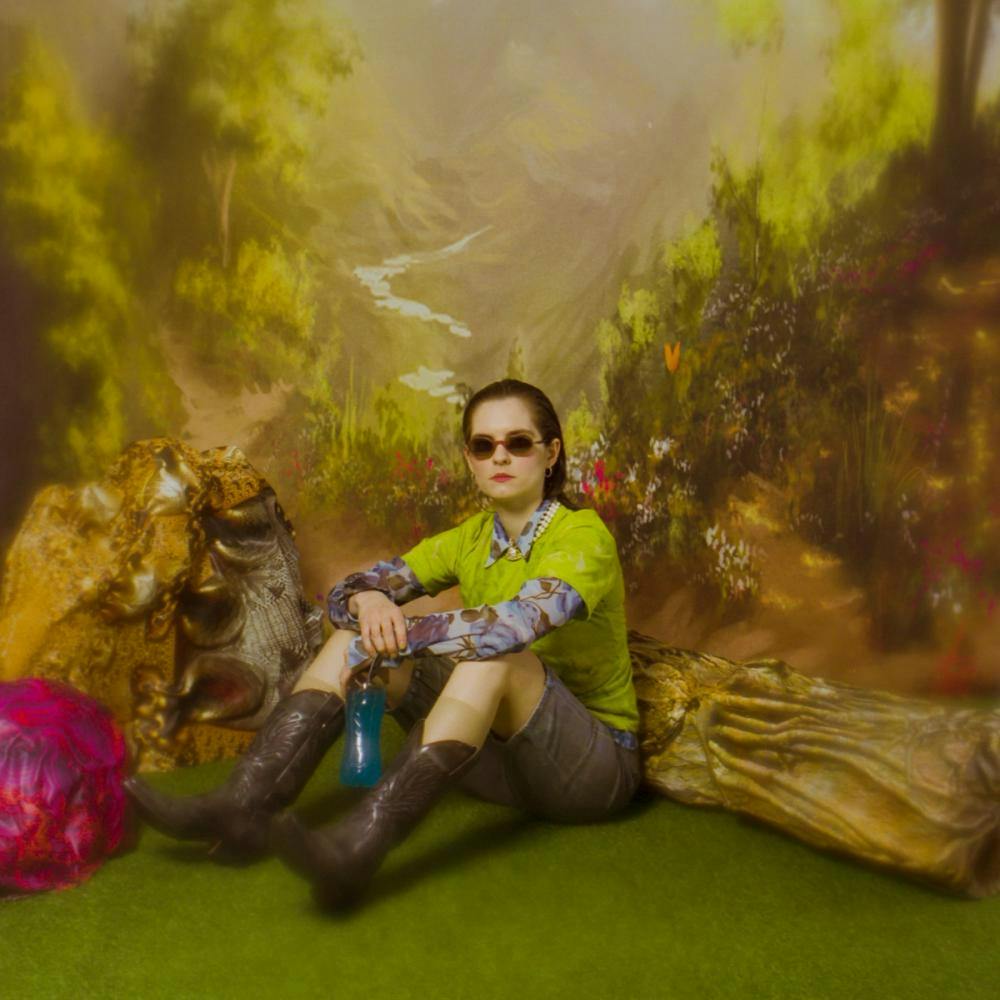 Künstlerin Fuffifufzich mit Sonnenbrille und Stiefel zentral sitzend vor malerischem Gemälde