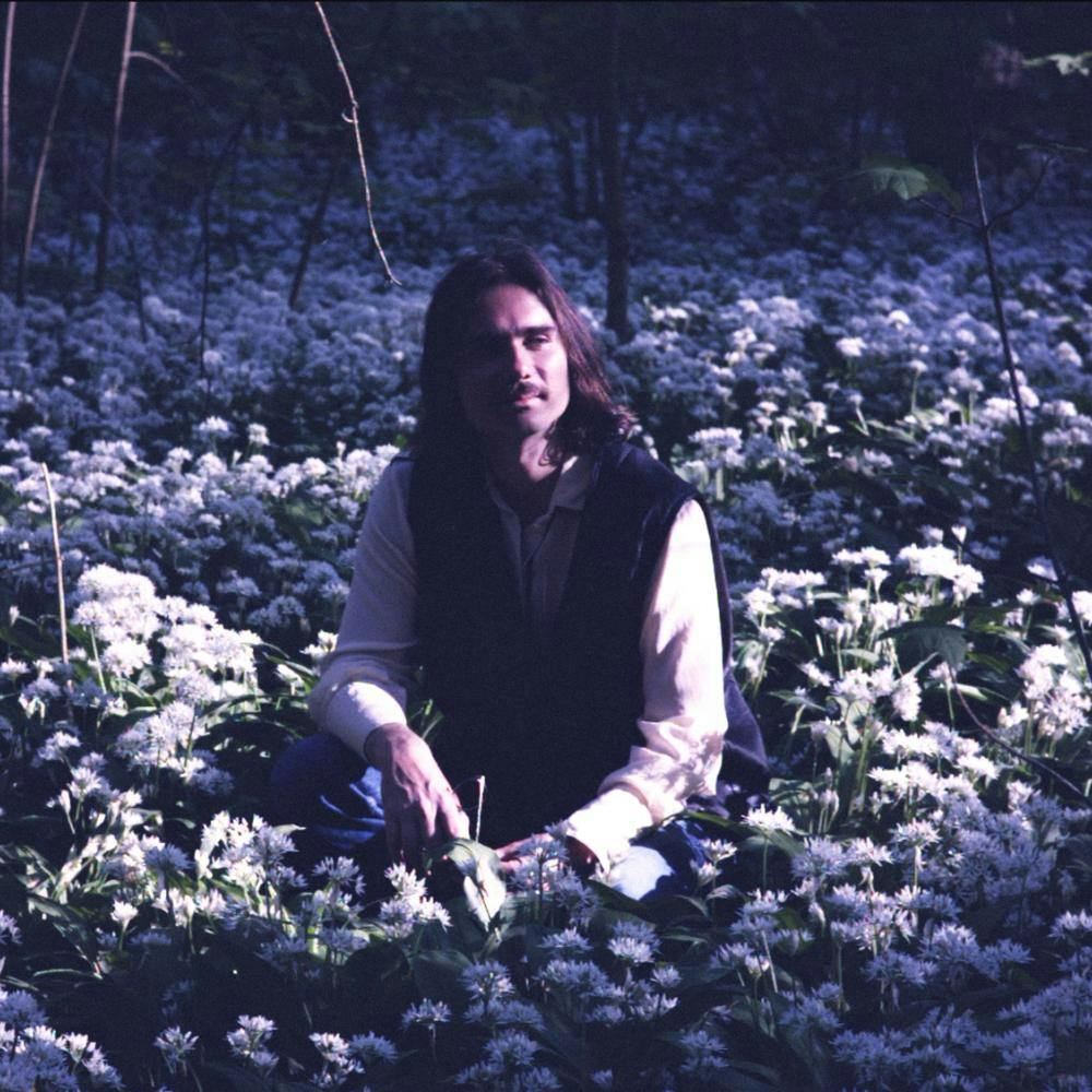Portrait von John Moods sitzend in Blumenfeld in leichten Blautönen
