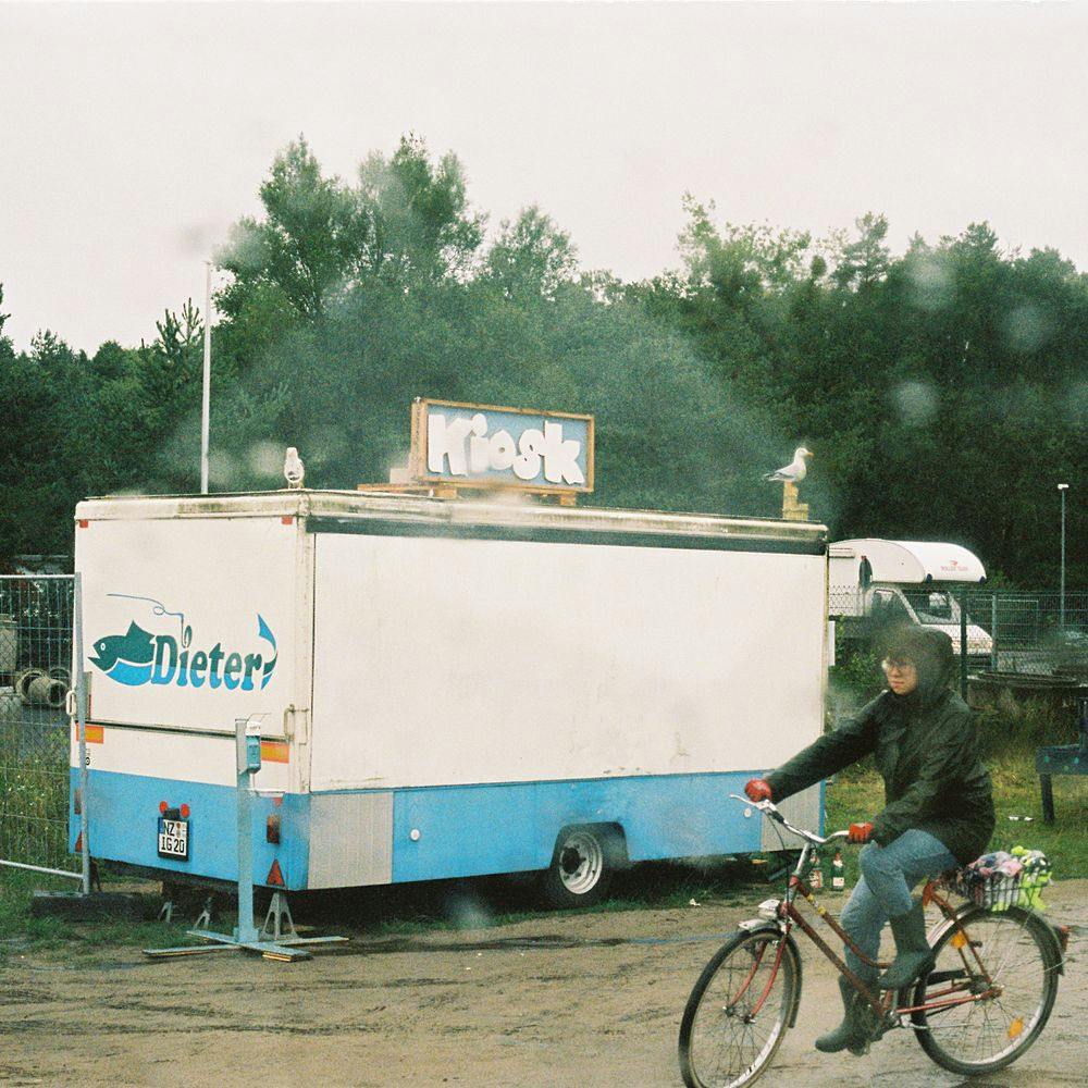 Kiosk "Dieter" mit Schild und eine Person auf dem Fahrrad bei Regen 