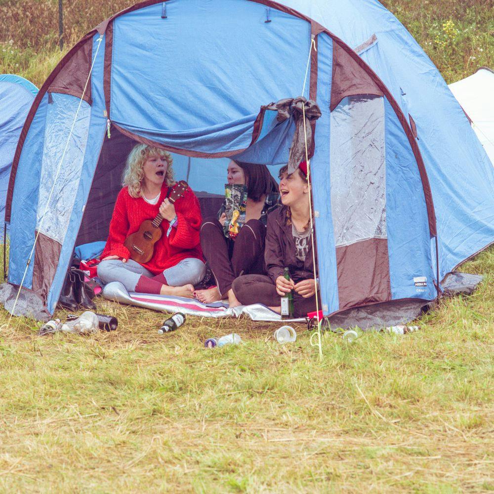Drei Personen mit Ukulele singend in einem Zelt