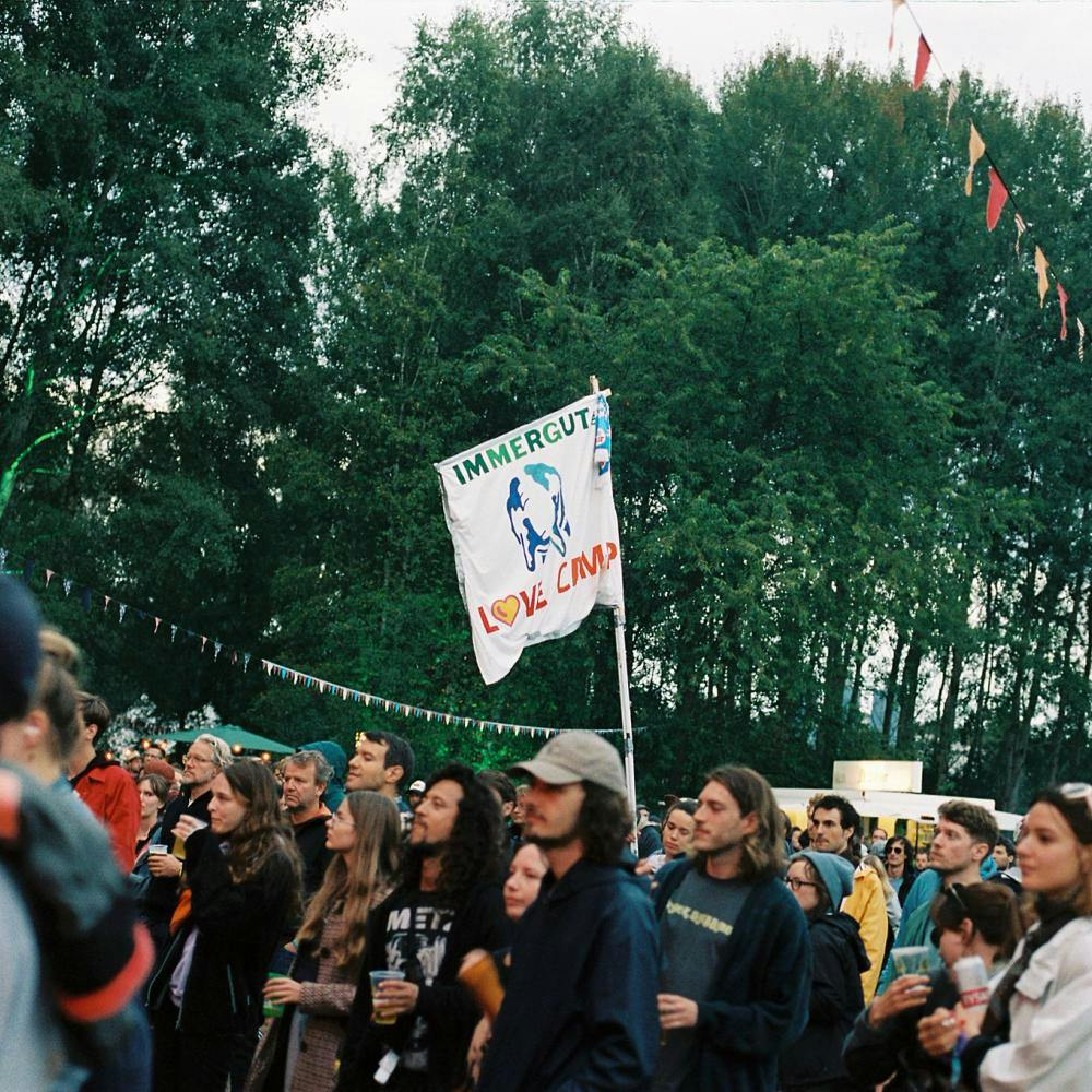 Blick in das Publikum vor der Feldbühne, mit Fahne mit Aufschrift "Immergut Love Camp"